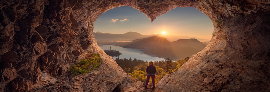 Young woman in heart shape cave towards the idyllic unrise